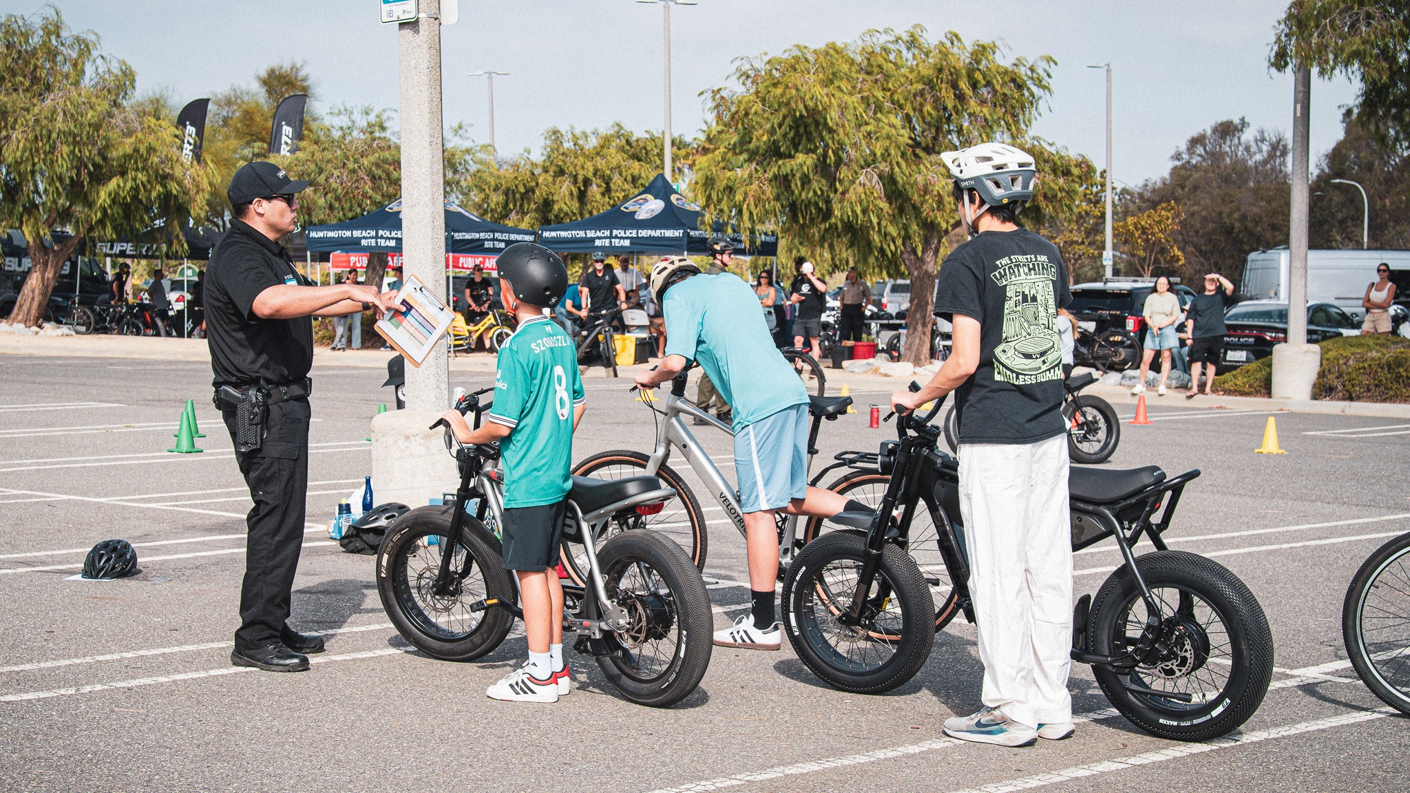 An officer briefing three helmeted young riders with their eBikes on a coned training course